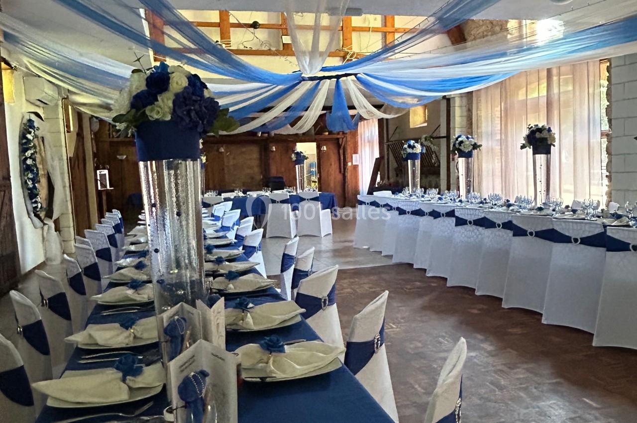 Salle de réception décorée de bleu et blanc avec des tables dressées et des arrangements floraux élégants.
