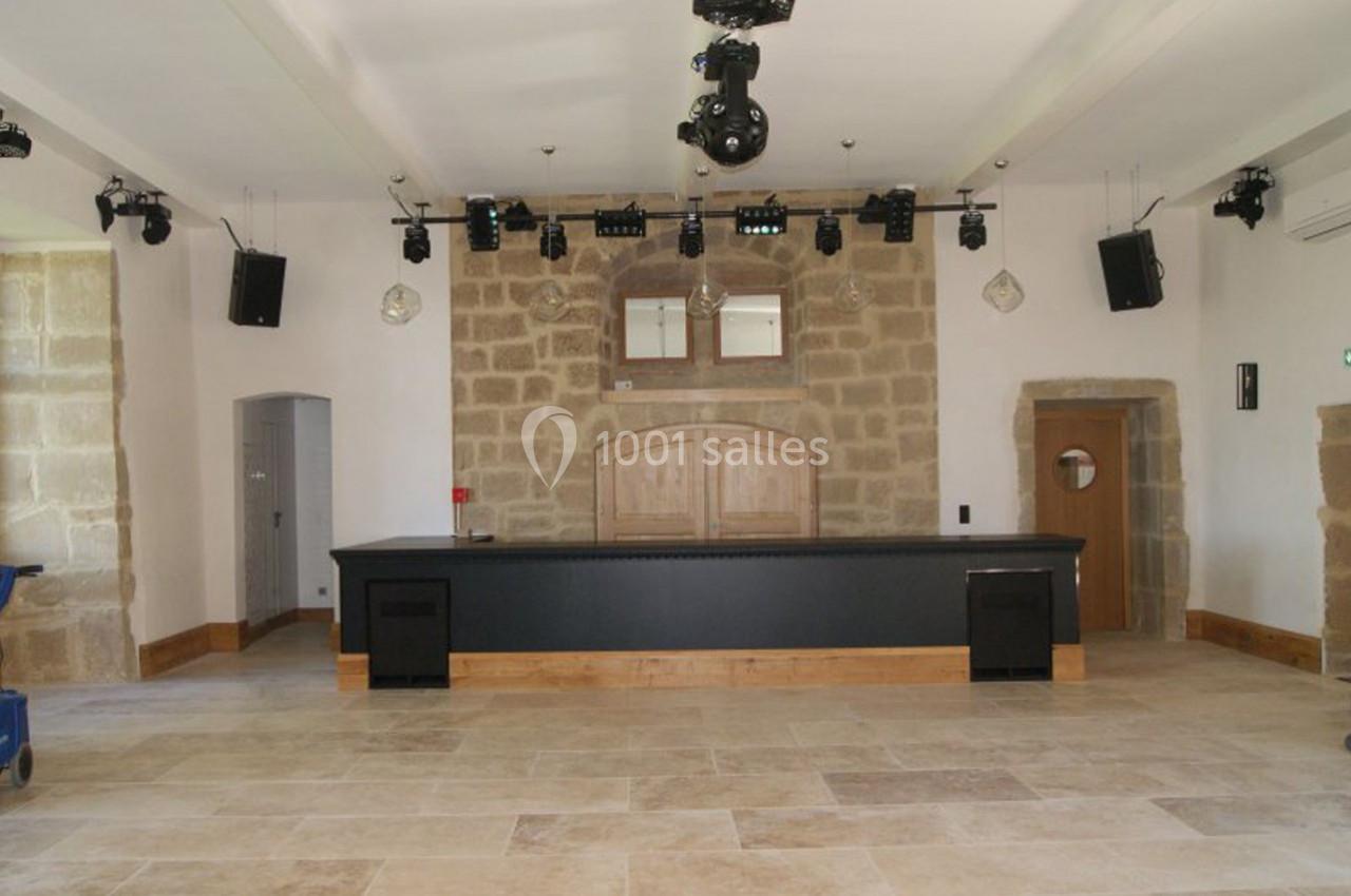 Salle avec un comptoir noir, murs en pierre, sol en carrelage clair, éclairages suspendus et équipements audio.