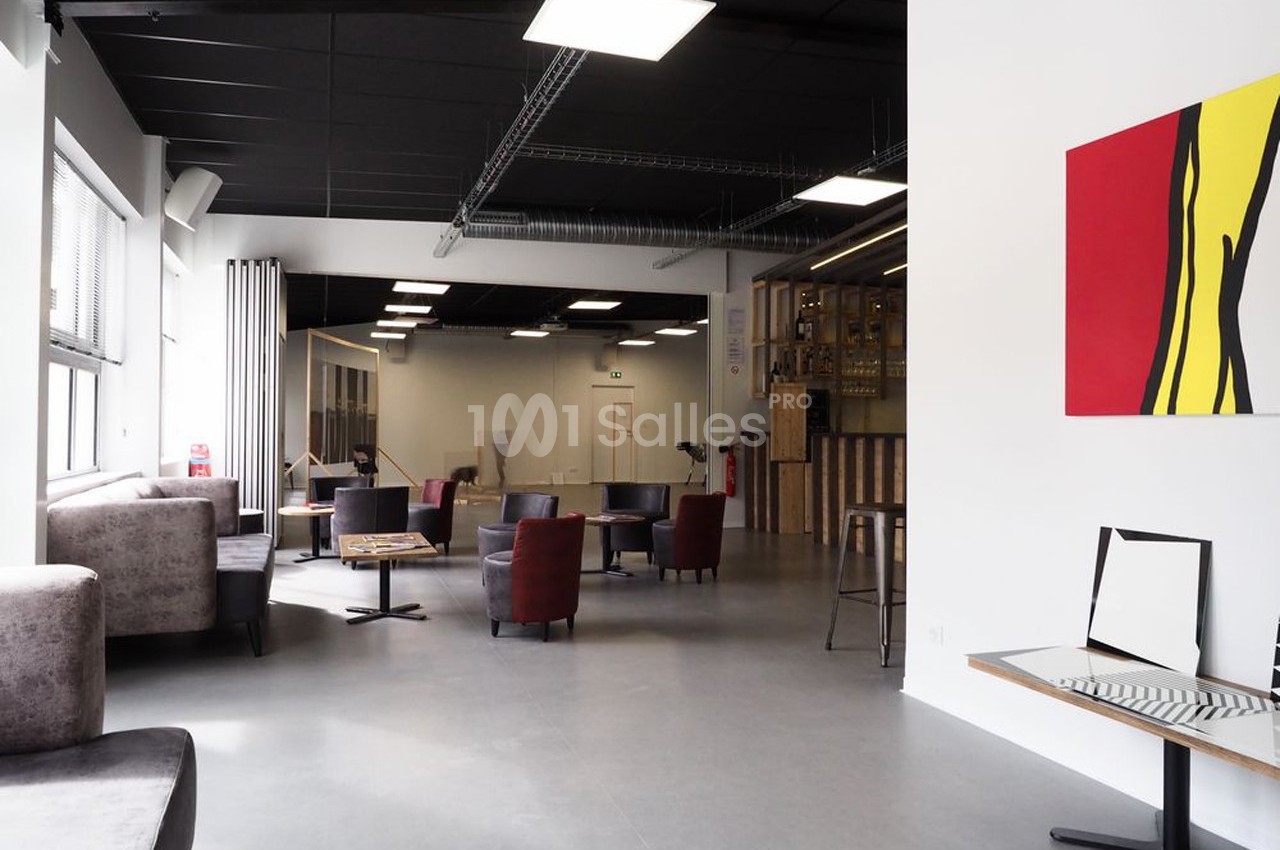Espace intérieur lumineux avec mobilier varié, murs blancs, tableau coloré et plafond noir industriel.