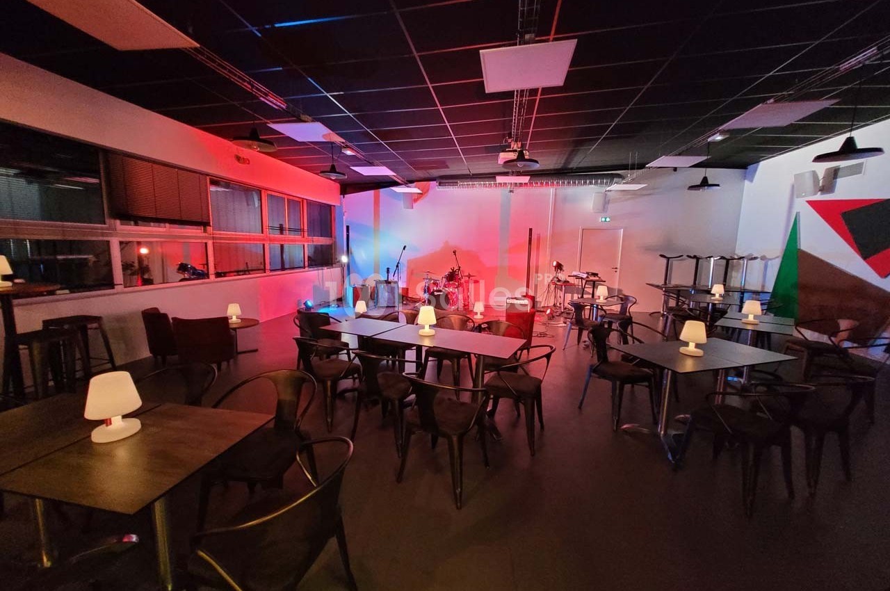 Salle de concert avec tables, chaises et éclairage coloré, scène équipée de micros et instruments de musique.