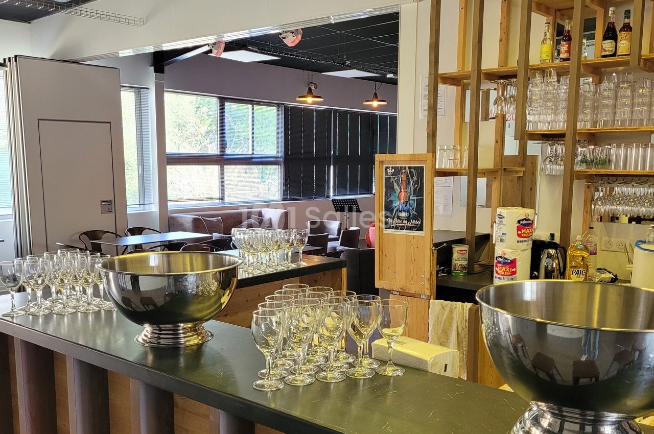 Un bar avec des verres et des seaux à champagne sur un comptoir, dans un espace lumineux avec des canapés en arrière-plan.