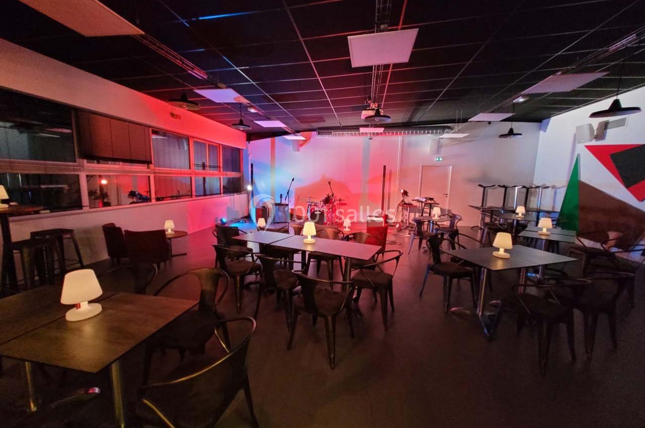Salle de concert avec tables, chaises et éclairage coloré, scène équipée de micros et instruments de musique.