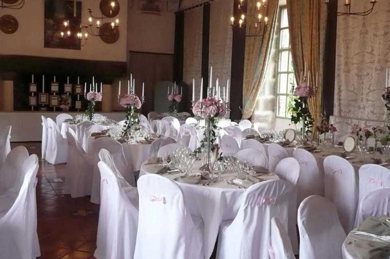 Salle de réception décorée avec des tables rondes, nappes blanches, chandeliers et bouquets de fleurs roses.