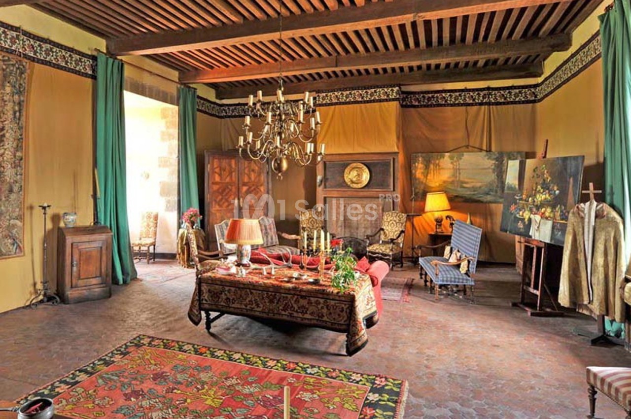 Salon ancien décoré avec des meubles en bois, tapis coloré, lustre, tableaux et rideaux verts.