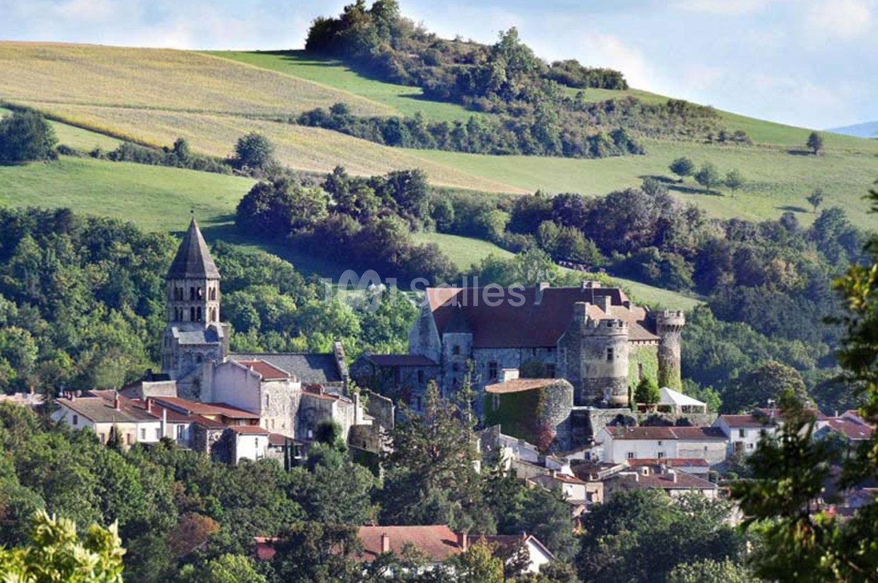 Vue d'un village avec une église, un château et des collines verdoyantes en arrière-plan.