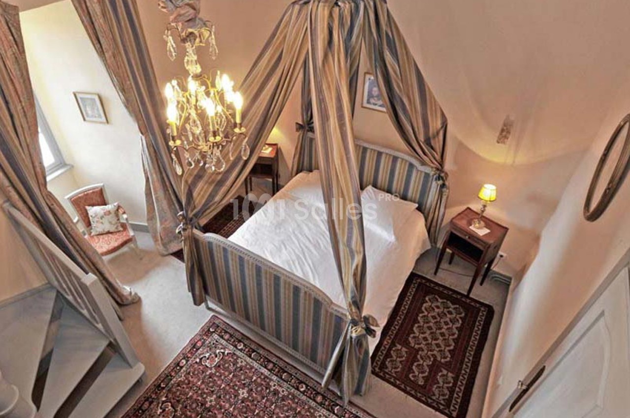 Lit à baldaquin rayé dans une chambre lumineuse avec tapis orientaux, lustre et tables de chevet.