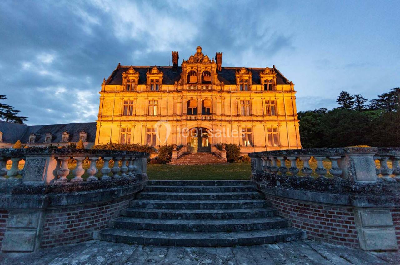 Façade d'un château illuminé au crépuscule, avec des escaliers en pierre et une balustrade au premier plan.