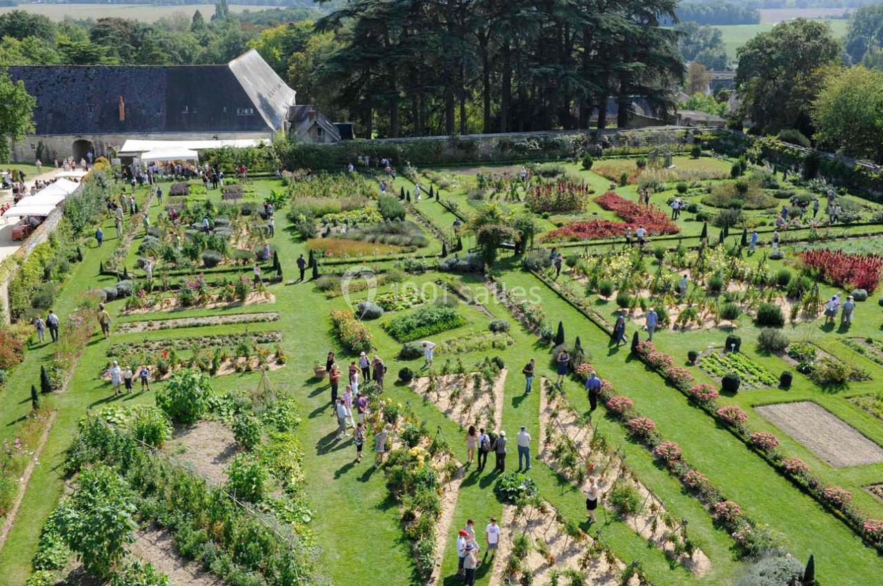 Vue aérienne d'un grand jardin potager avec des visiteurs se promenant parmi les allées et les plantations variées.