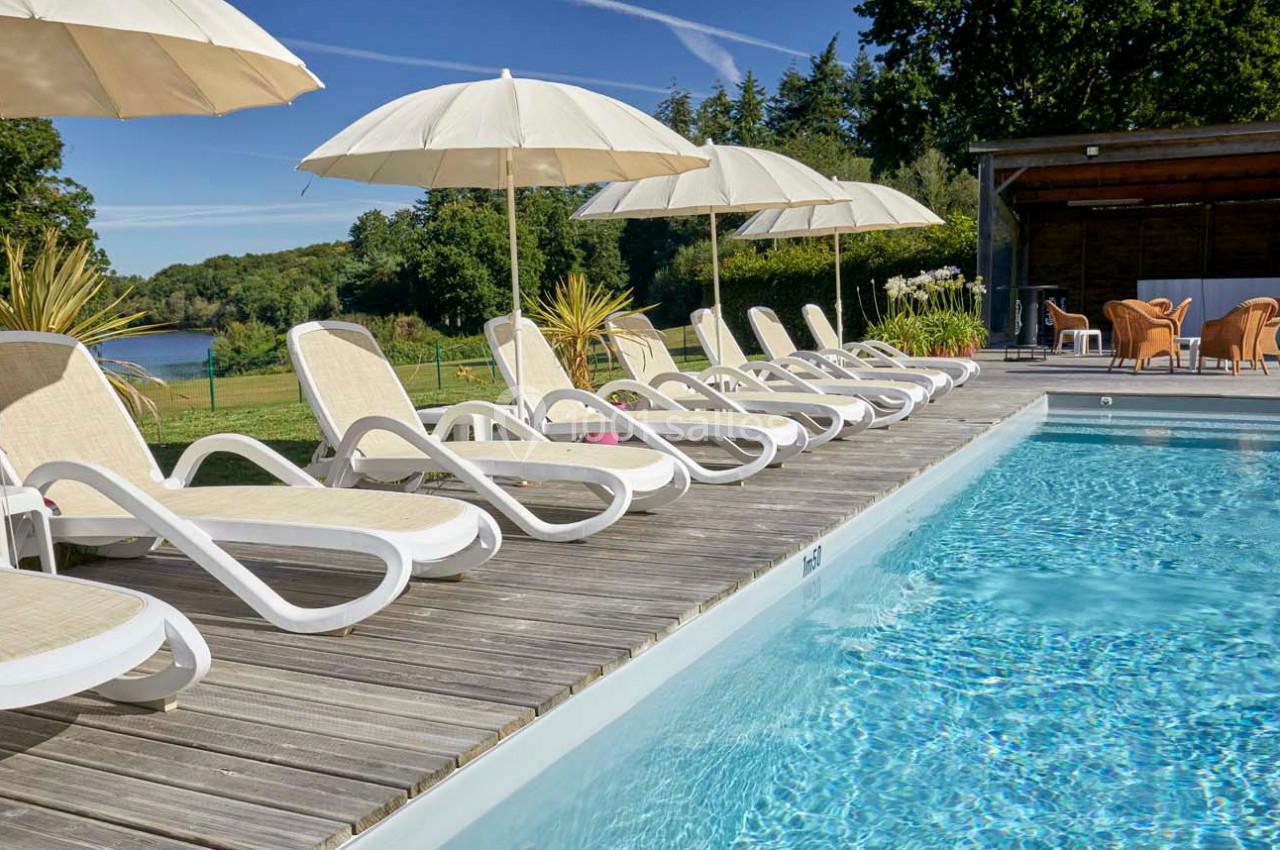 Chaises longues et parasols alignés autour d'une piscine extérieure, avec vue sur un paysage verdoyant.