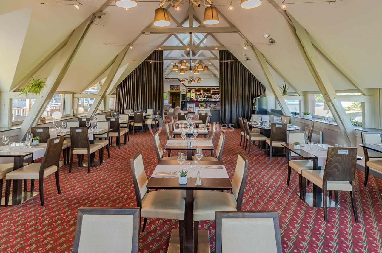 Salle de restaurant lumineuse avec tables dressées, chaises en bois et plafond en poutres apparentes.