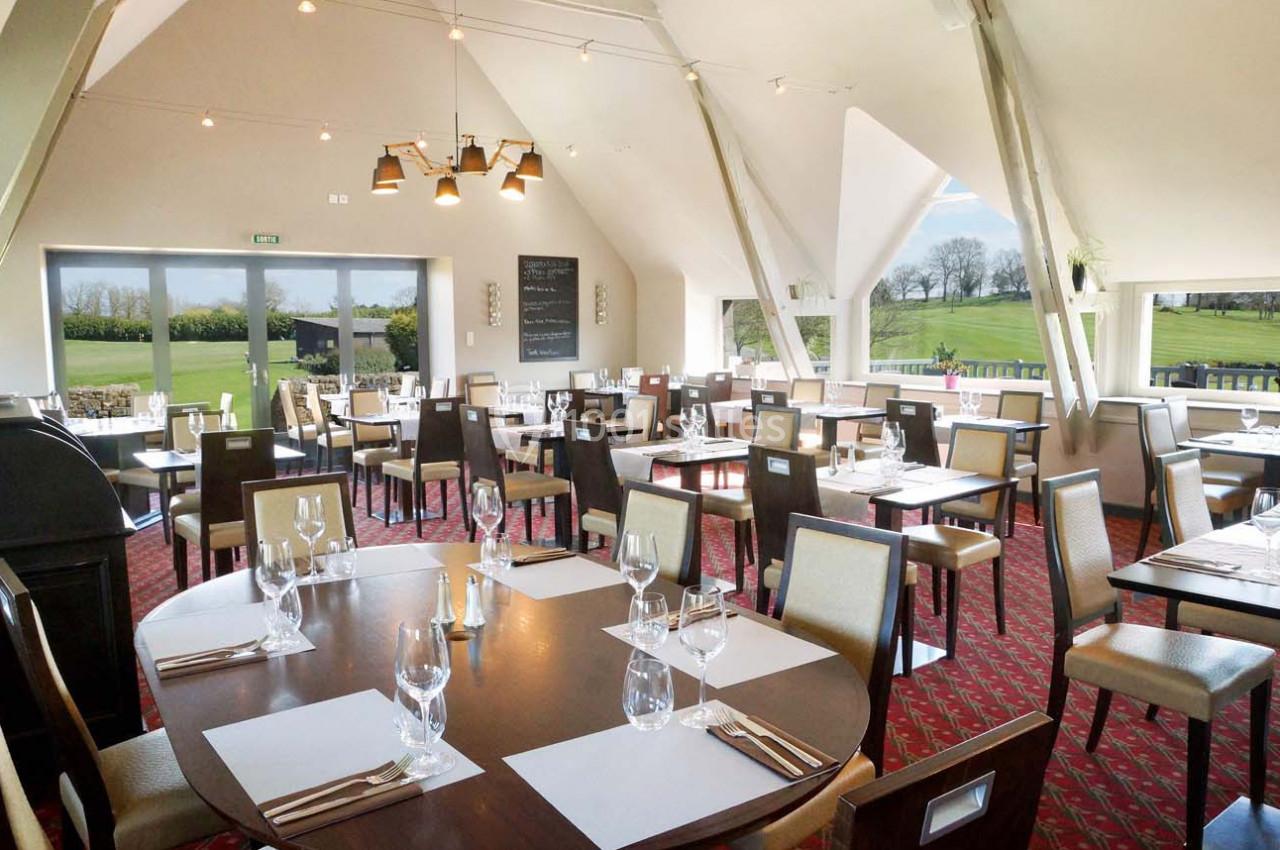 Salle de restaurant lumineuse avec grandes fenêtres donnant sur un paysage verdoyant, tables dressées avec élégance.