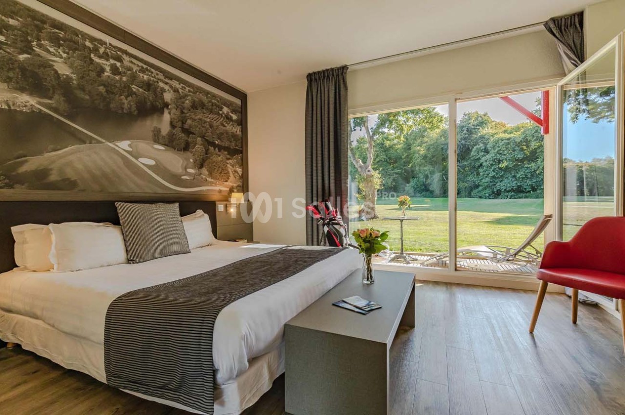 Chambre lumineuse avec lit double, grande baie vitrée donnant sur un jardin verdoyant et terrasse aménagée.