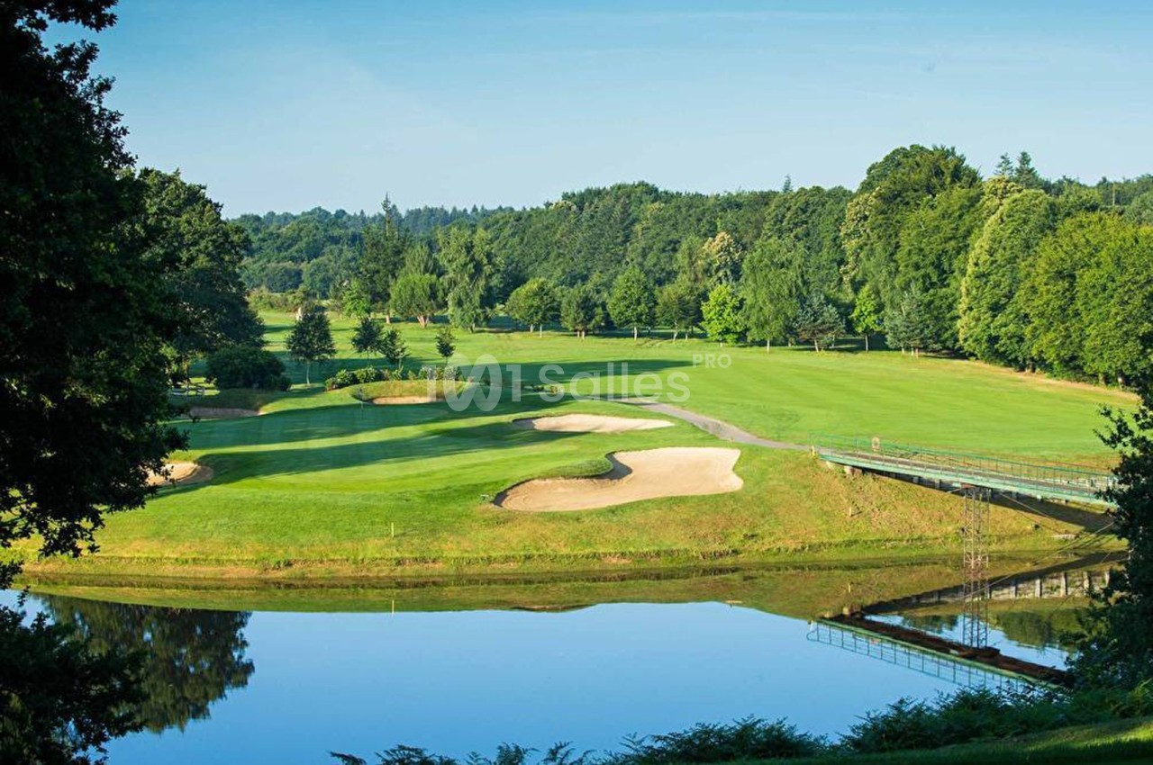 Vue d'un terrain de golf verdoyant avec bunkers, un pont et un plan d'eau entouré d'arbres.