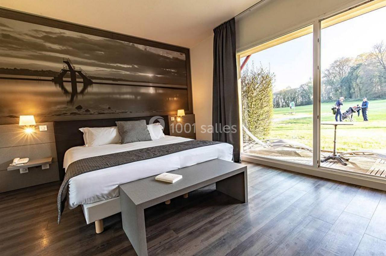 Chambre lumineuse avec grand lit, décor mural, parquet, et vue sur un terrain de golf à travers une baie vitrée.