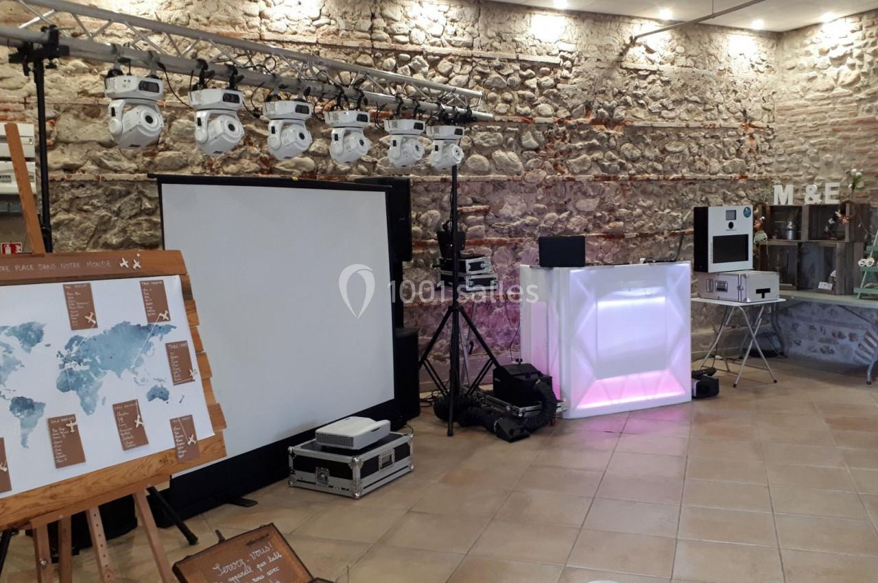 Salle décorée pour un événement avec éclairage, cabine DJ, carte du monde sur chevalet et mur en pierres apparentes.