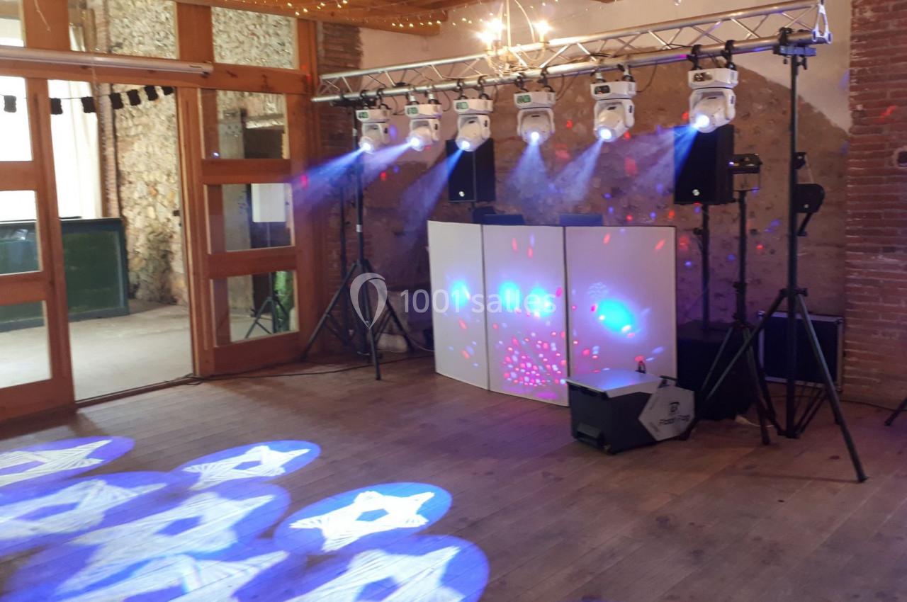 Installation de matériel d'éclairage et de sonorisation dans une salle avec murs en pierre et parquet en bois.