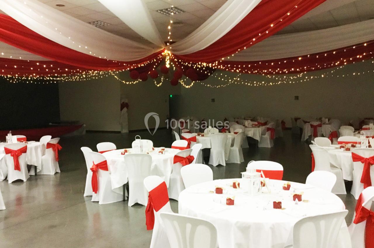 Salle de réception décorée de nappes blanches et rouges, avec des guirlandes lumineuses suspendues au plafond.