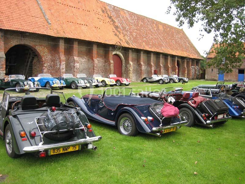 Voitures anciennes alignées sur une pelouse devant un bâtiment en briques avec toit en tuiles rouges.