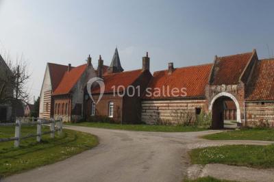Miniature Location salle Clairmarais (Pas-de-Calais) - La Ferme de l'Abbaye #17 Façade d'une grange en briques avec porte en bois rouge, toit en tuiles et piles de bois empilées sur les côtés.