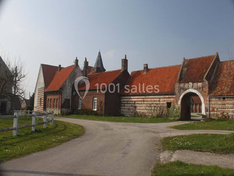 Bâtiments anciens en briques et pierres avec toits en tuiles rouges, entourés d'un chemin et d'espaces verts.