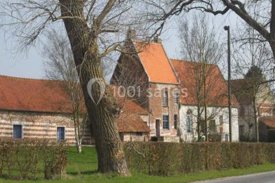 Miniature Location salle Clairmarais (Pas-de-Calais) - La Ferme de l'Abbaye #16 Façade d'une grange en briques avec porte en bois rouge, toit en tuiles et piles de bois empilées sur les côtés.