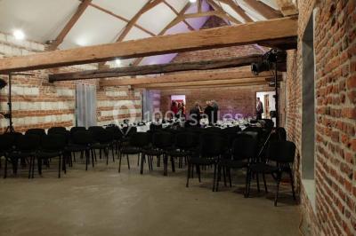 Miniature Location salle Clairmarais (Pas-de-Calais) - La Ferme de l'Abbaye #10 Façade d'une grange en briques avec porte en bois rouge, toit en tuiles et piles de bois empilées sur les côtés.