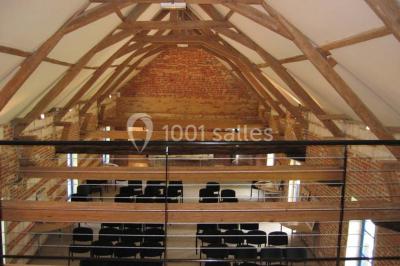 Miniature Location salle Clairmarais (Pas-de-Calais) - La Ferme de l'Abbaye #9 Façade d'une grange en briques avec porte en bois rouge, toit en tuiles et piles de bois empilées sur les côtés.