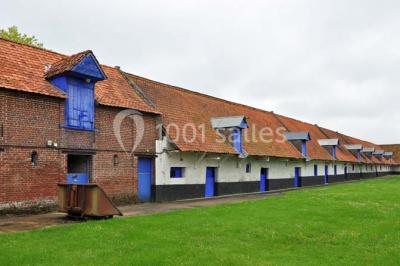 Miniature Location salle Clairmarais (Pas-de-Calais) - La Ferme de l'Abbaye #14 Façade d'une grange en briques avec porte en bois rouge, toit en tuiles et piles de bois empilées sur les côtés.