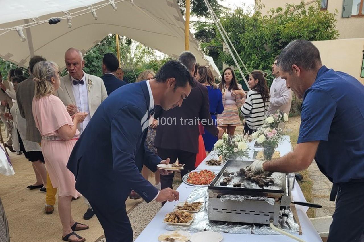 Des convives se servent à un buffet en plein air avec un cuisinier préparant des plats sur une plancha.