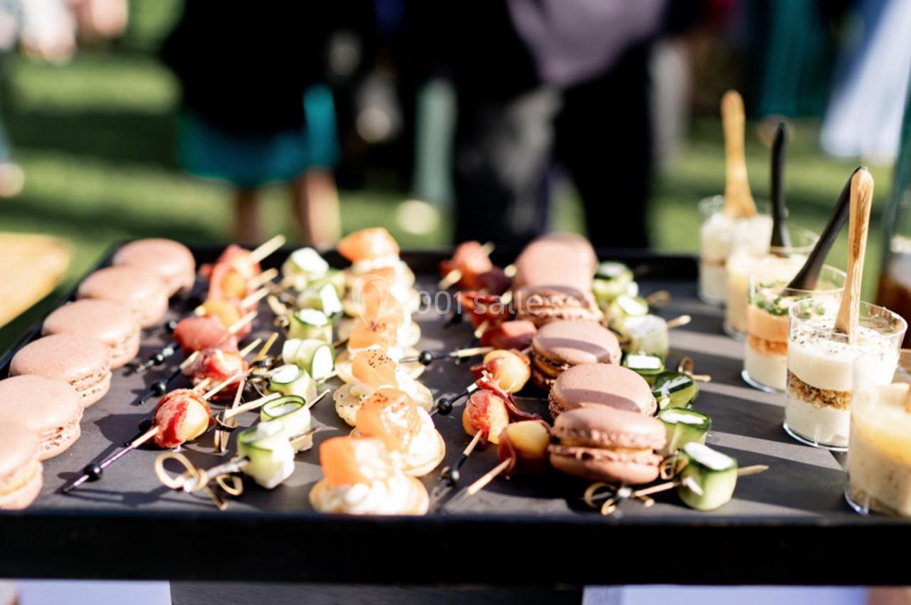 Plateau de bouchées apéritives variées comprenant macarons, brochettes de légumes et verrines, présenté en extérieur.