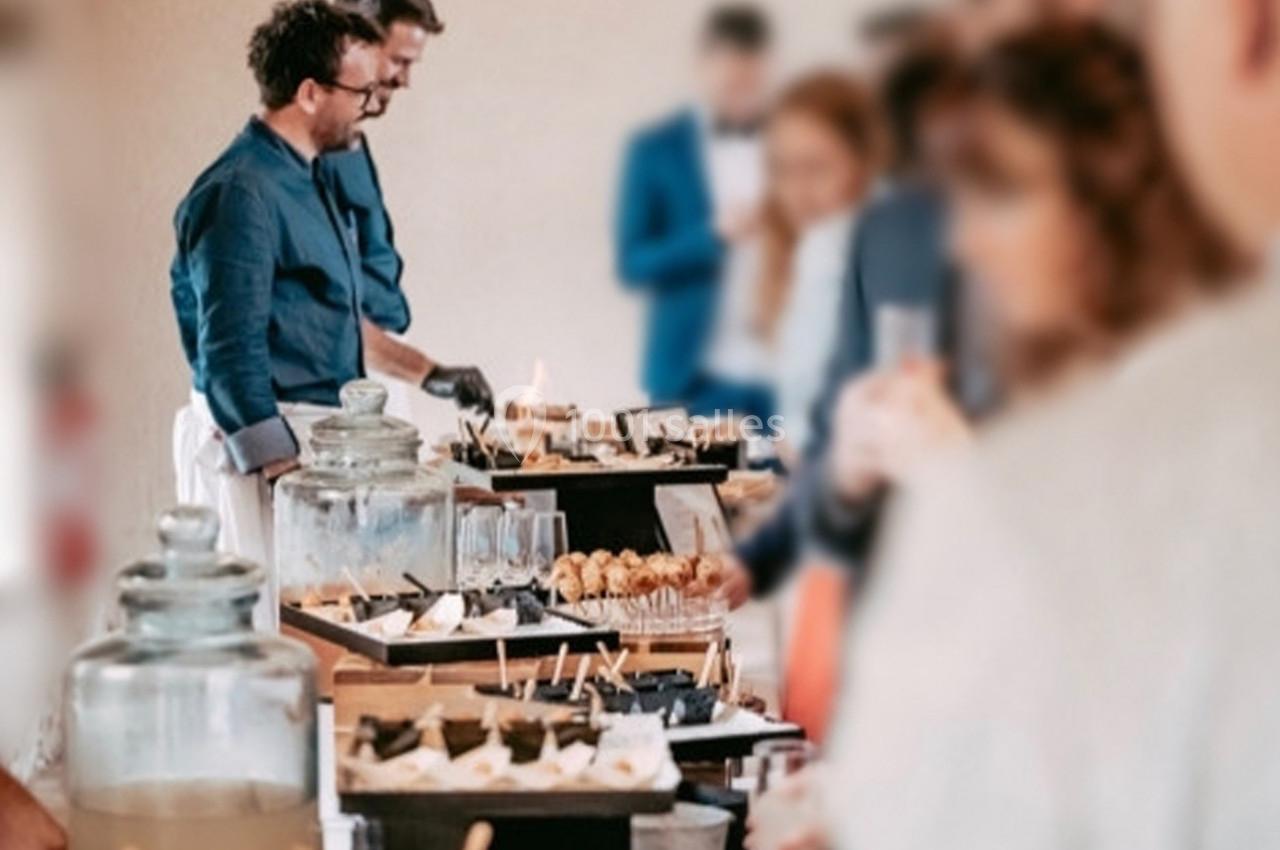 Buffet avec desserts variés, boissons et convives en arrière-plan dans un cadre convivial.