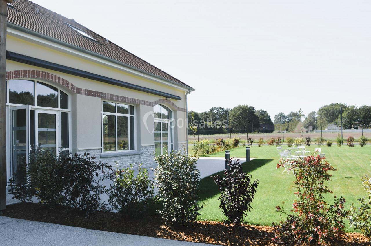 Bâtiment avec de grandes fenêtres donnant sur un jardin aménagé avec pelouse et quelques arbustes.
