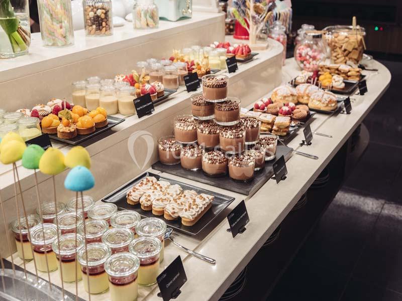Buffet de desserts variés avec verrines, pâtisseries, fruits et brochettes colorées sur une table éclairée.