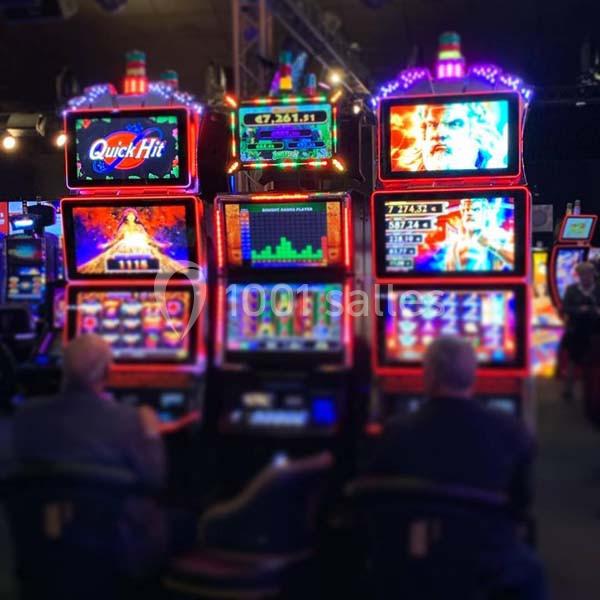 Deux personnes jouent sur des machines à sous lumineuses dans une salle de jeux.