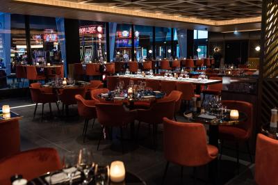 Salle de restaurant moderne avec des tables dressées, des chaises orange et un éclairage chaleureux.