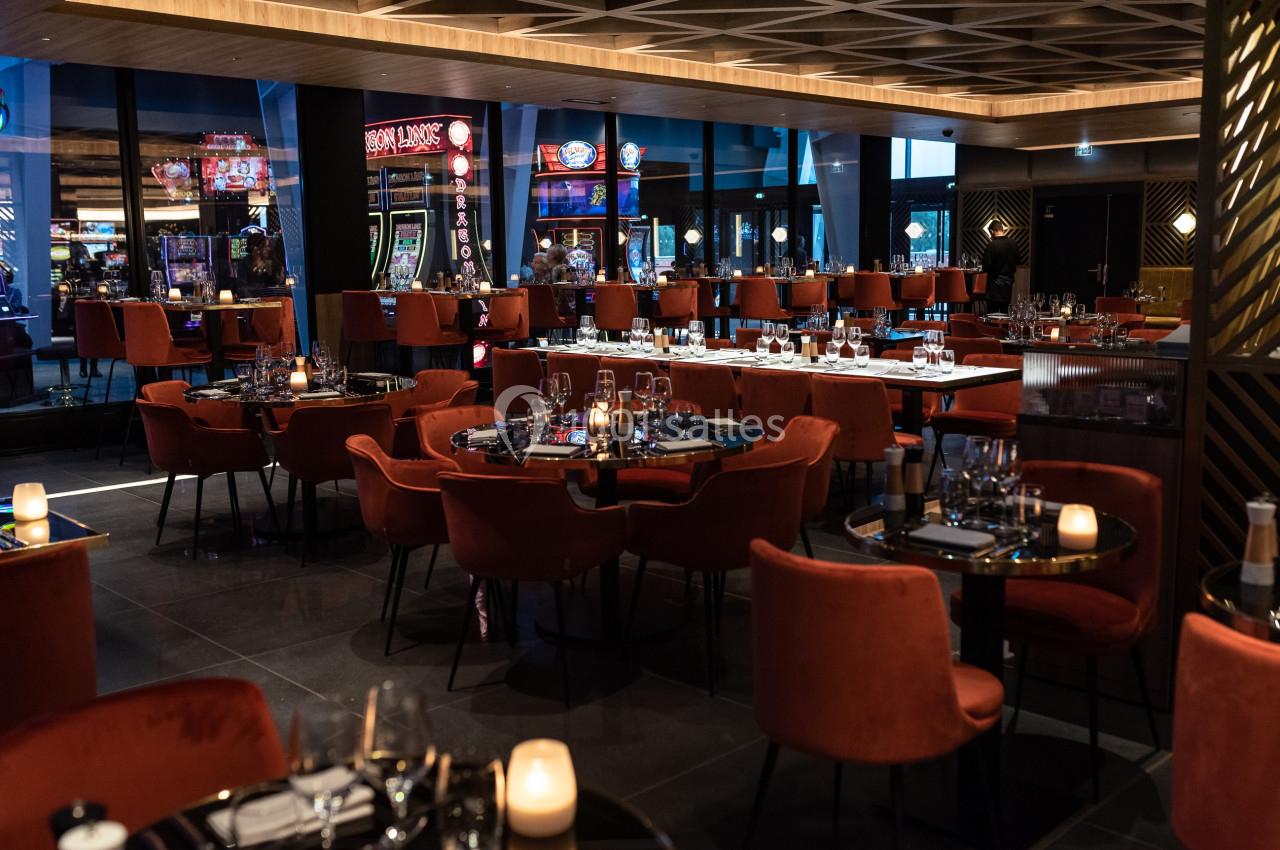 Salle de restaurant élégante avec des tables dressées, des chaises rouges et une ambiance tamisée.