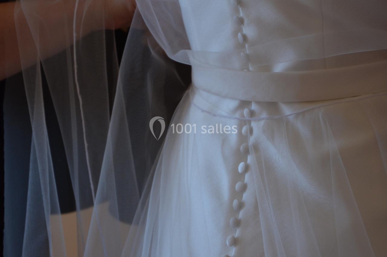 Robe de mariée en satin blanc avec boutons recouverts et voile transparent drapé.