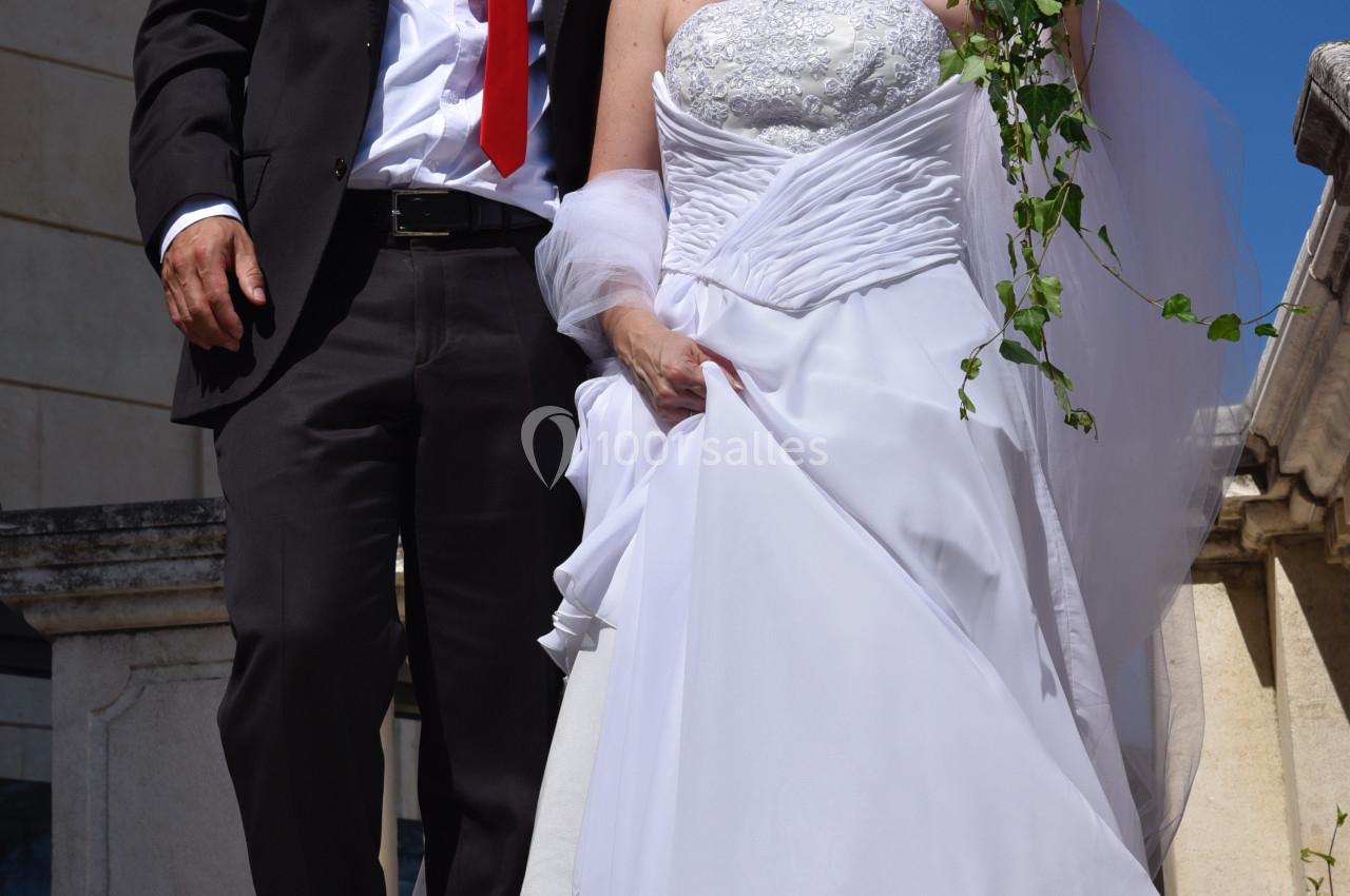 Un couple en tenue de mariage descend un escalier en pierre par une journée ensoleillée.