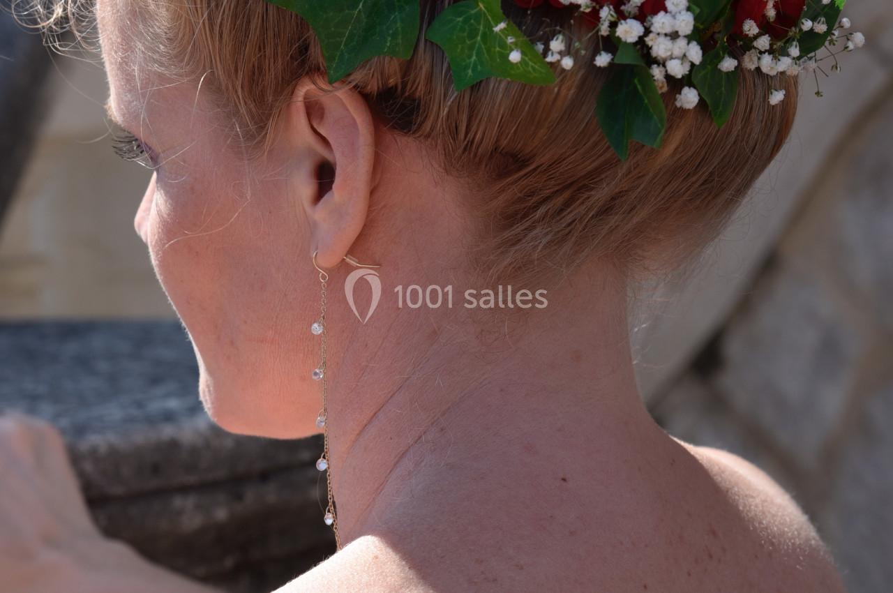 Coiffure de mariage avec chignon orné de fleurs rouges, gypsophile et feuillage, vue de dos en extérieur.