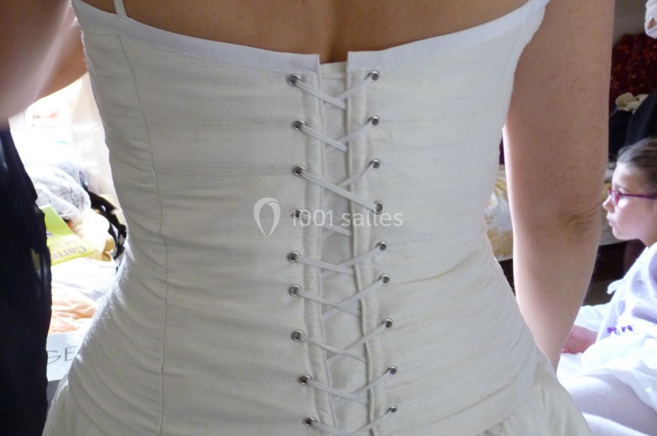 Dos d'une femme portant une robe de mariée blanche avec un corset lacé, vue dans un environnement intérieur.