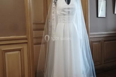 Miniature Claire Avias Créations #20 Mannequin vêtu d'une robe en dentelle blanche avec un voile noir couvrant la tête, devant une porte en bois clair.