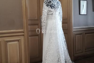 Miniature Claire Avias Créations #21 Mannequin vêtu d'une robe en dentelle blanche avec un voile noir couvrant la tête, devant une porte en bois clair.