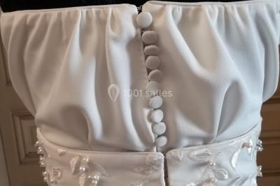 Miniature Claire Avias Créations #23 Mannequin vêtu d'une robe en dentelle blanche avec un voile noir couvrant la tête, devant une porte en bois clair.