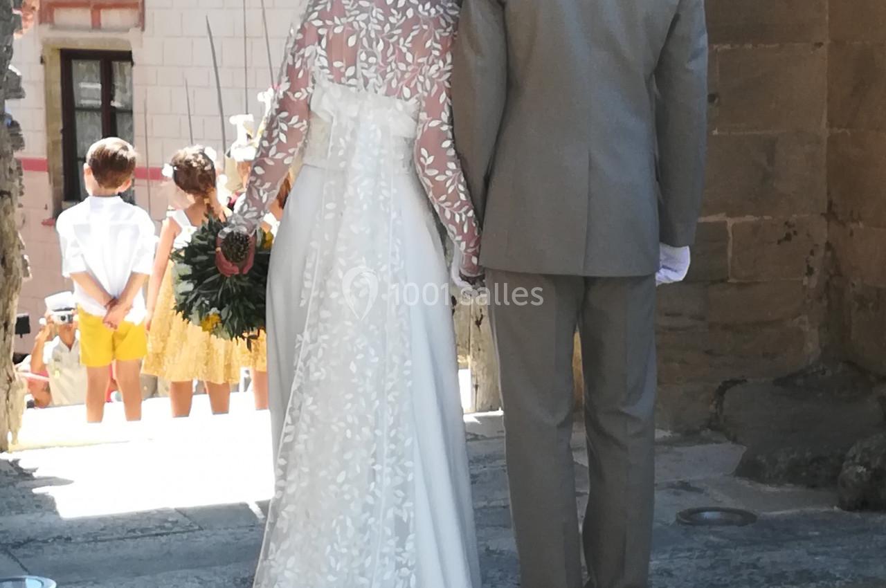 Un couple en tenue de mariage vu de dos, sortant d'un bâtiment ancien, avec des enfants en arrière-plan.