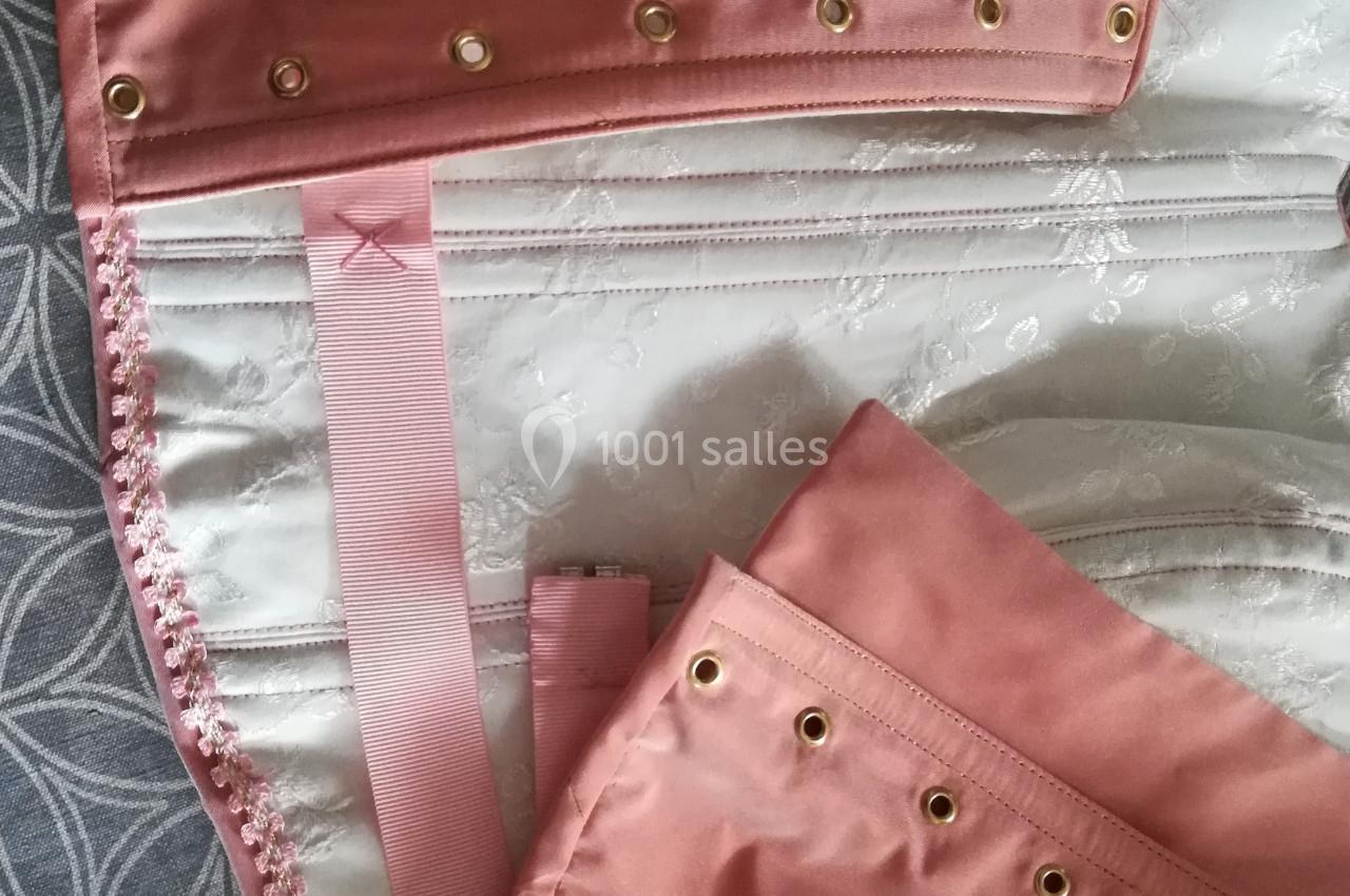 Vue rapprochée d'un corset rose en satin avec œillets dorés et rubans, posé sur un tissu à motifs.