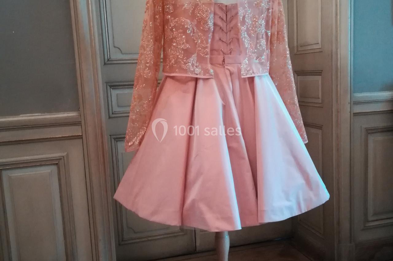 Robe rose avec jupe évasée et haut brodé transparent, présentée sur un mannequin dans un intérieur élégant.