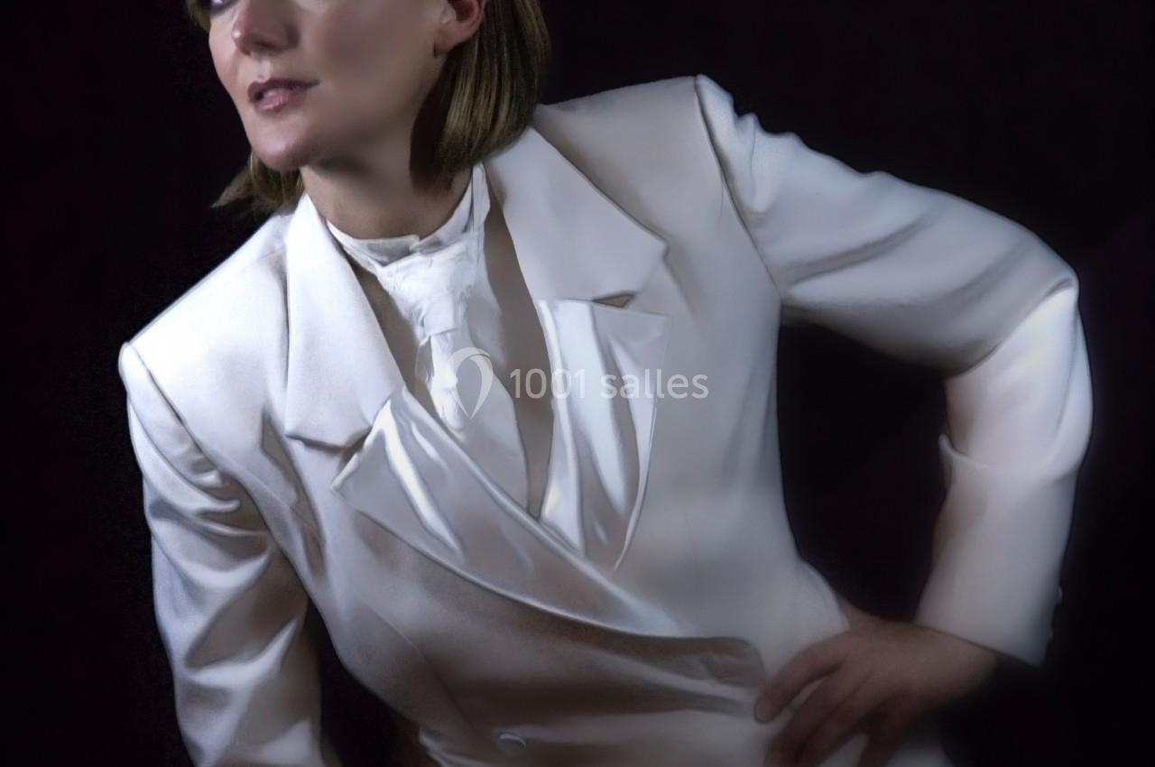 Personne posant dans un costume blanc élégant sur un fond sombre, regard tourné vers le côté.