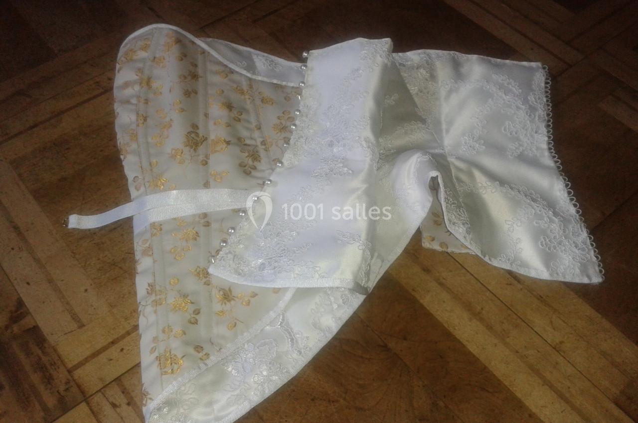 Corset blanc et doré en dentelle et tissu satiné, posé sur un sol en parquet.