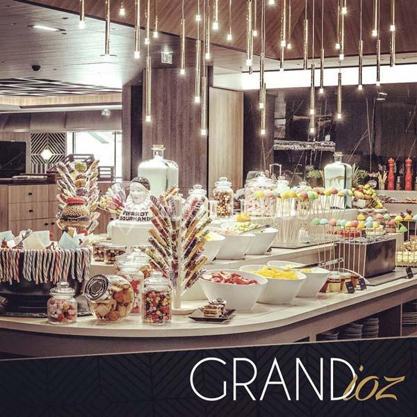 Buffet coloré avec desserts, bonbons, fruits et décorations lumineuses dans un espace moderne et élégant.