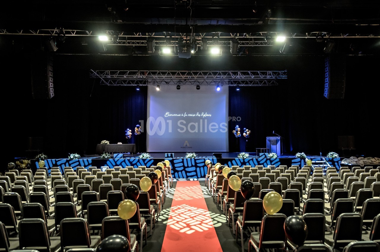 Salle de conférence aménagée avec des rangées de chaises, un écran de projection et une décoration festive.